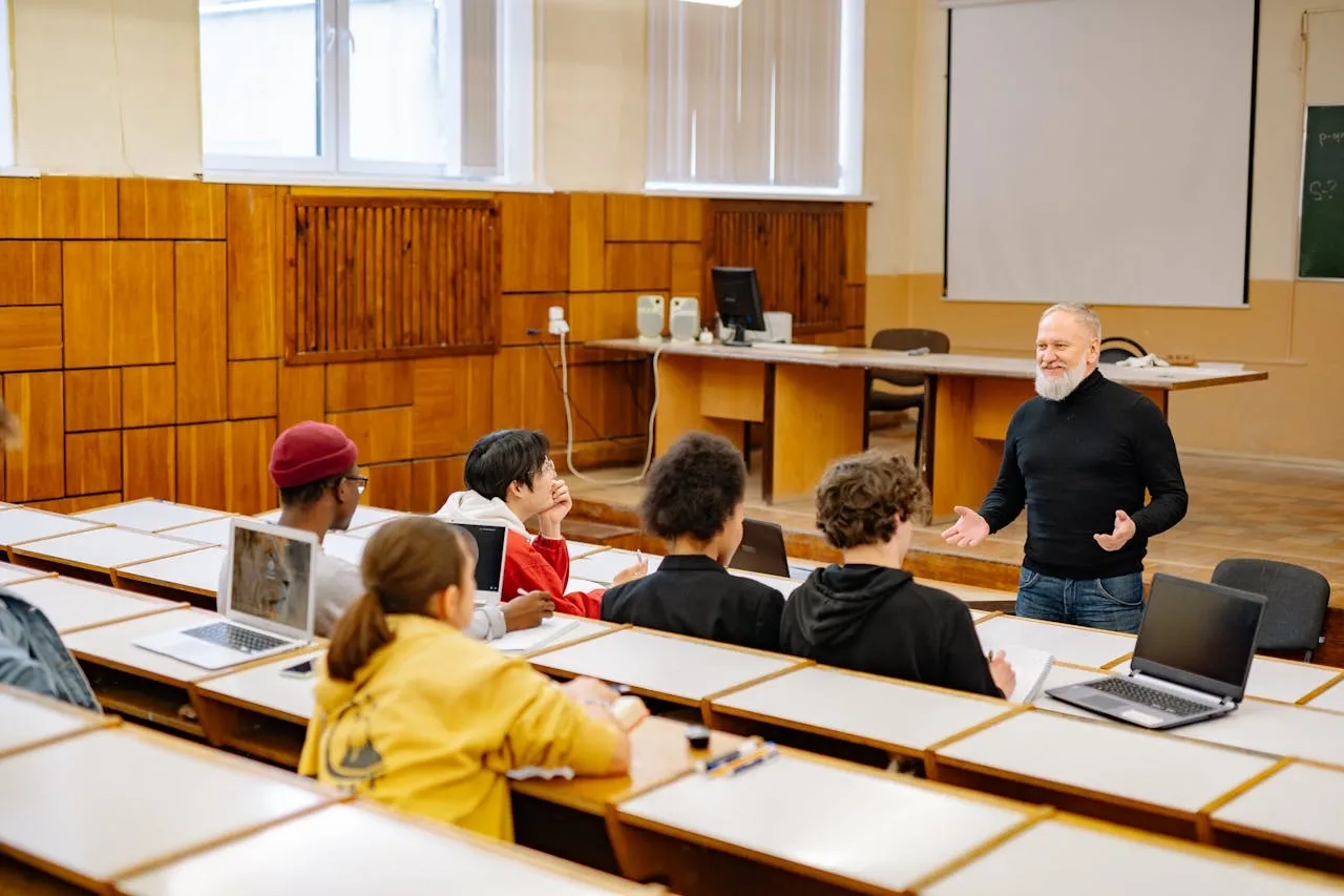 Professor teaching his student during a lecture, students also have laptop on desk.