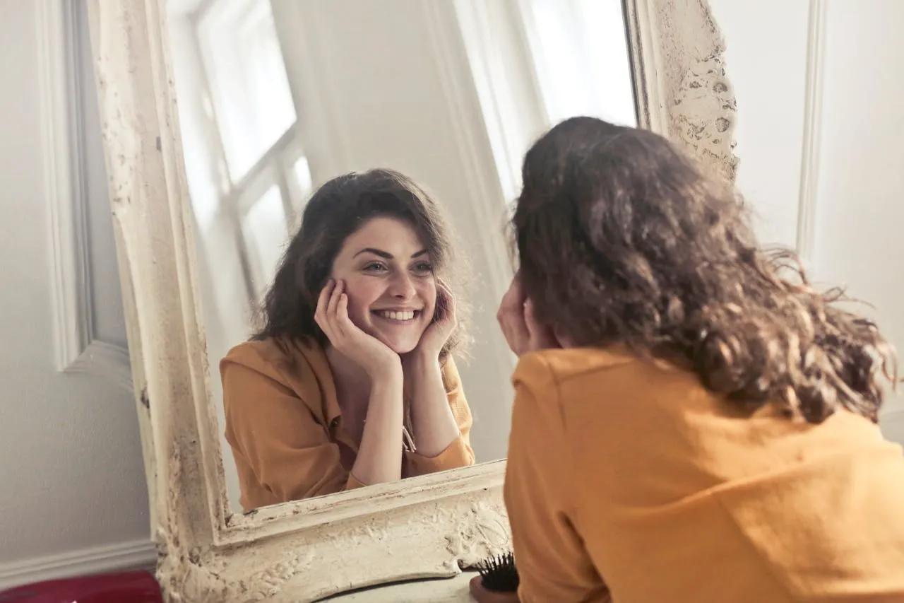A lady with a cheerful smile looking at her in mirror